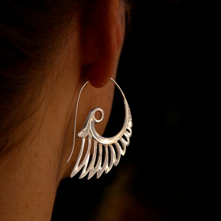 Silver earrings worn on an ear with a dark background