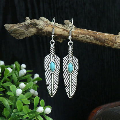Feather-shaped earrings with turquoise stones on a branch against a dark background