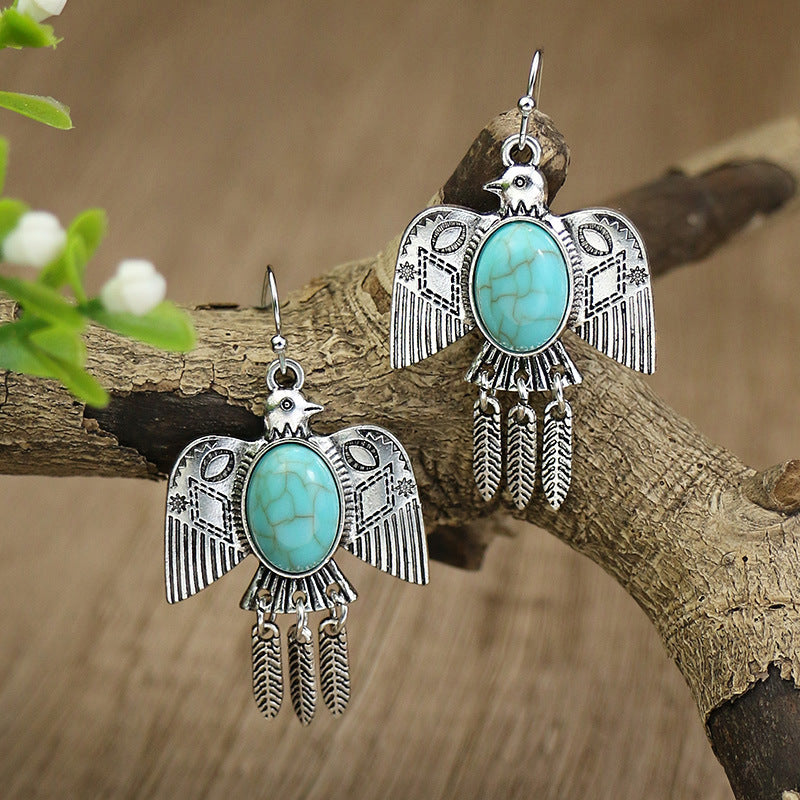 Silver bird-shaped earrings with turquoise stones on a wooden branch