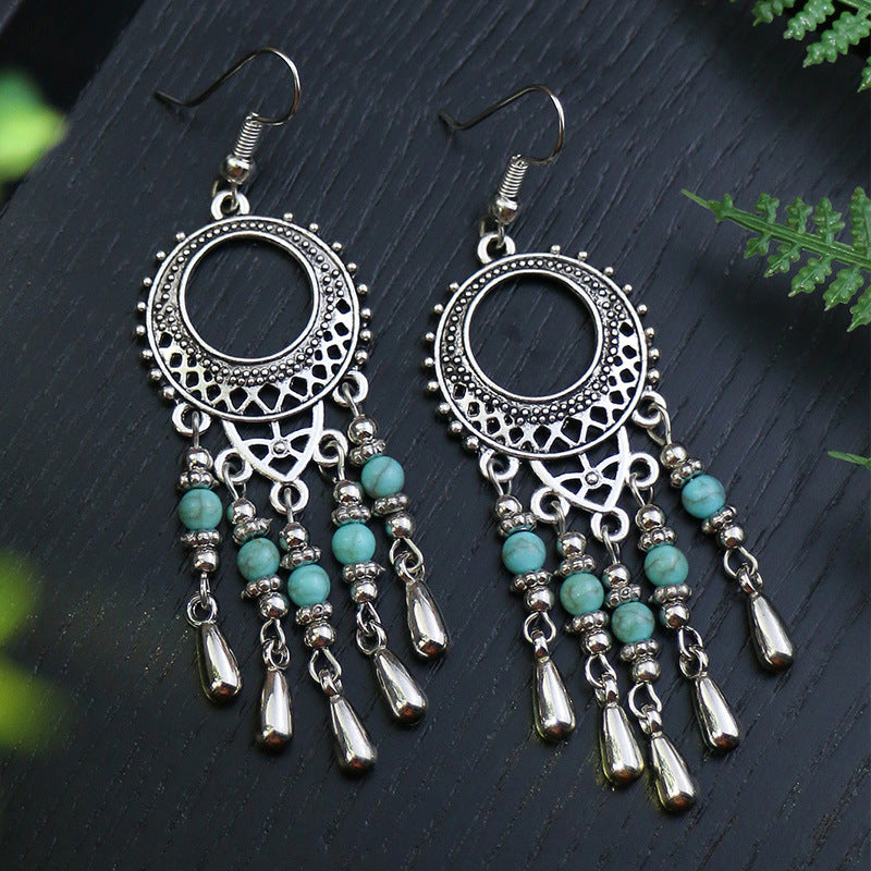 Pair of silver and turquoise earrings on a dark surface with green leaves.