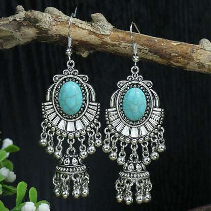 Pair of silver earrings with turquoise stones on a branch against a dark background