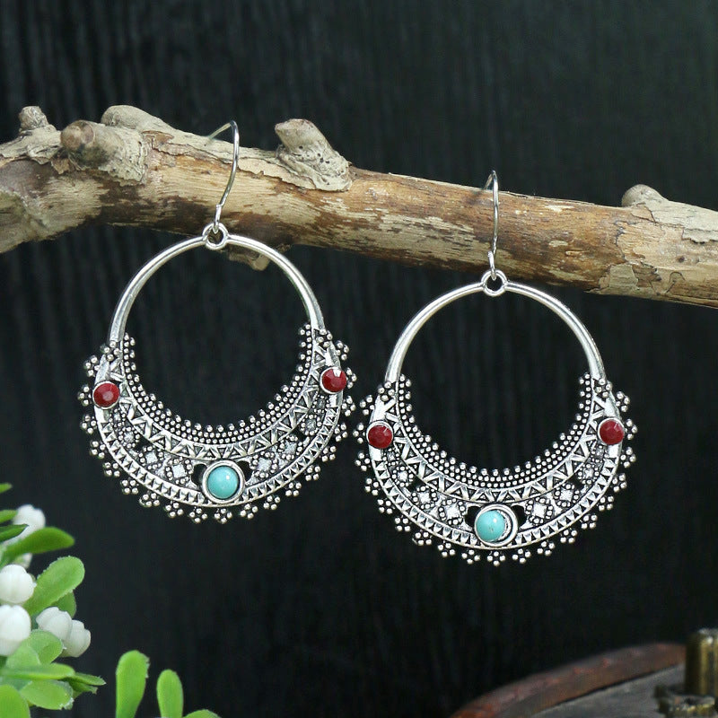 Silver hoop earrings with red and turquoise stones on a branch against a dark background
