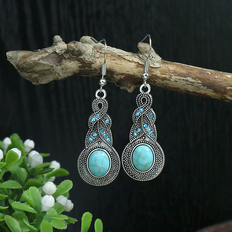 Pair of silver earrings with turquoise stones on a branch with greenery