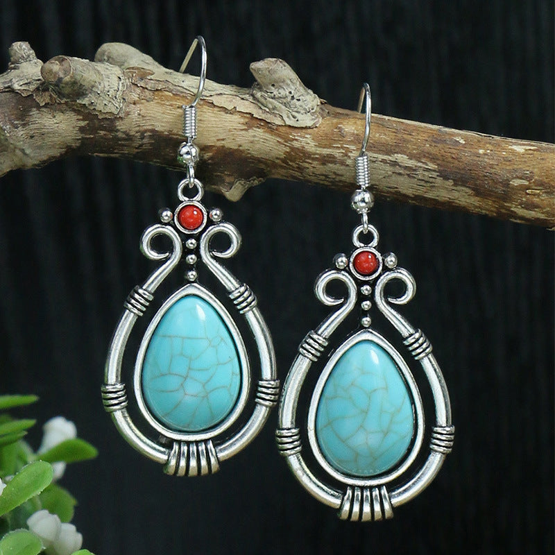 Turquoise teardrop earrings with silver wire wrapping and red stones on a branch against a dark background.